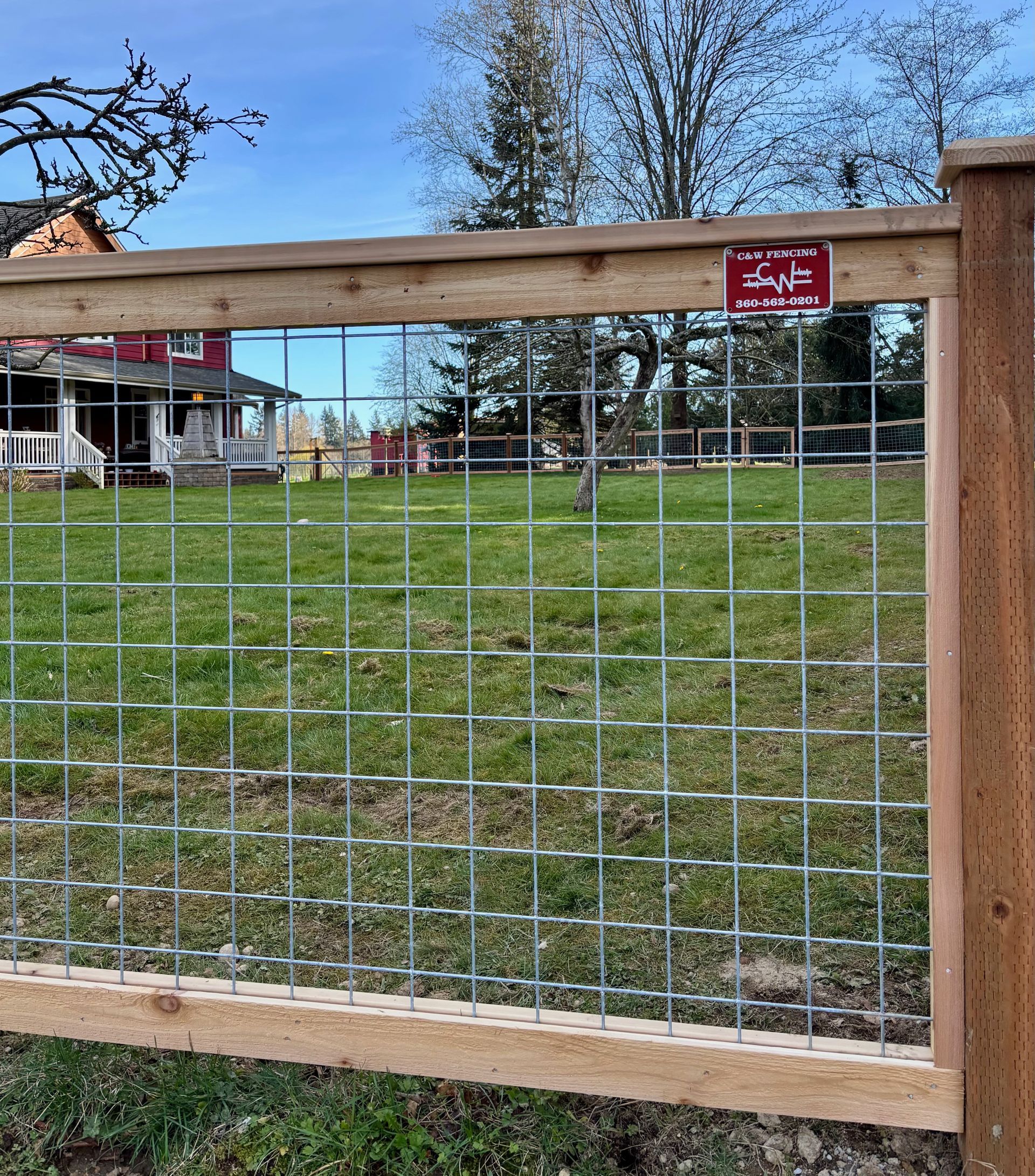 Wooden and wire fence around a grassy yard with houses and trees in the background