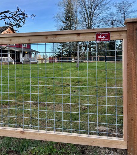 Wooden and wire fence around a grassy yard with houses and trees in the background