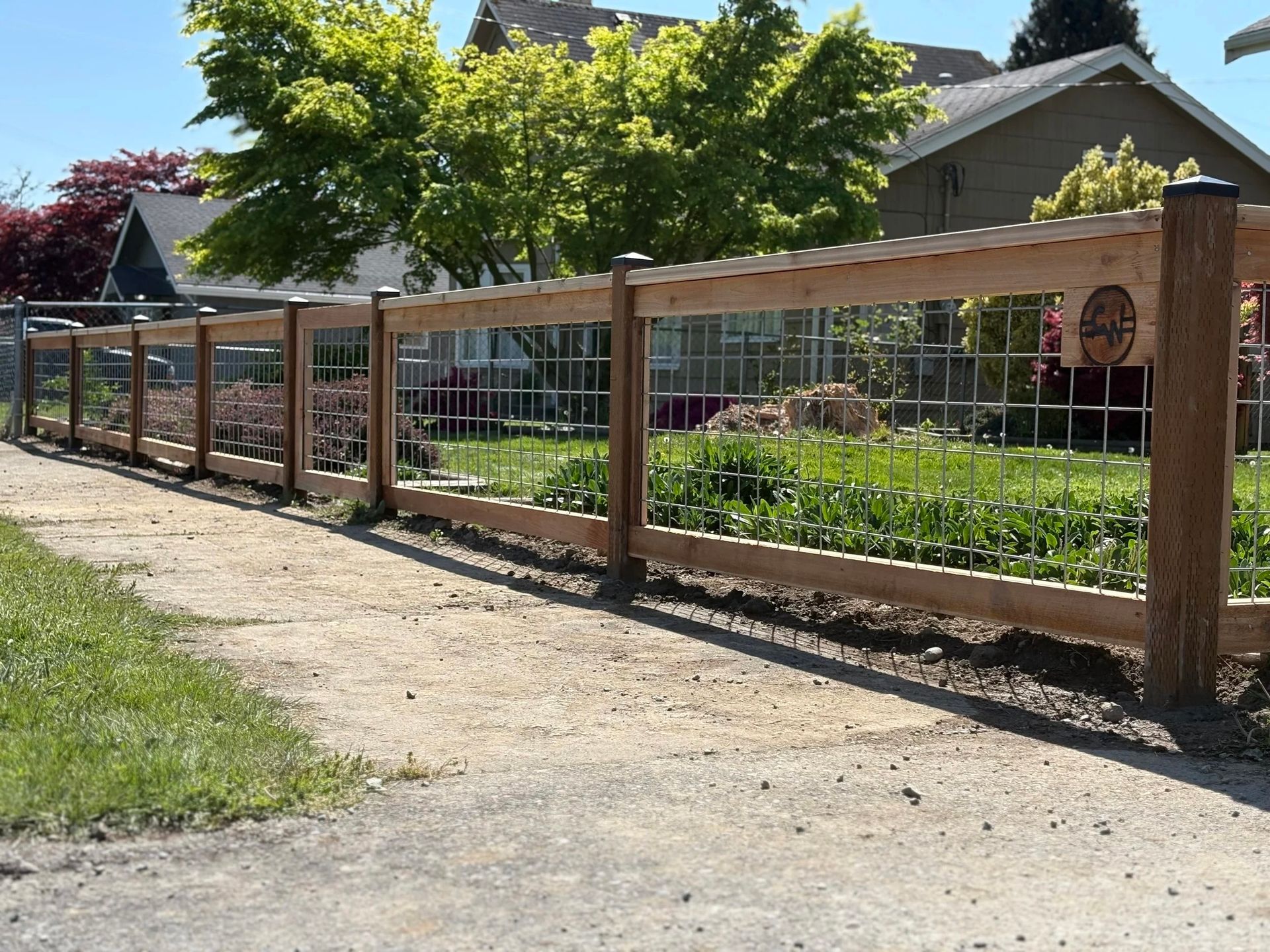 Wooden fence along a gravel path beside a garden and house in bright daylight