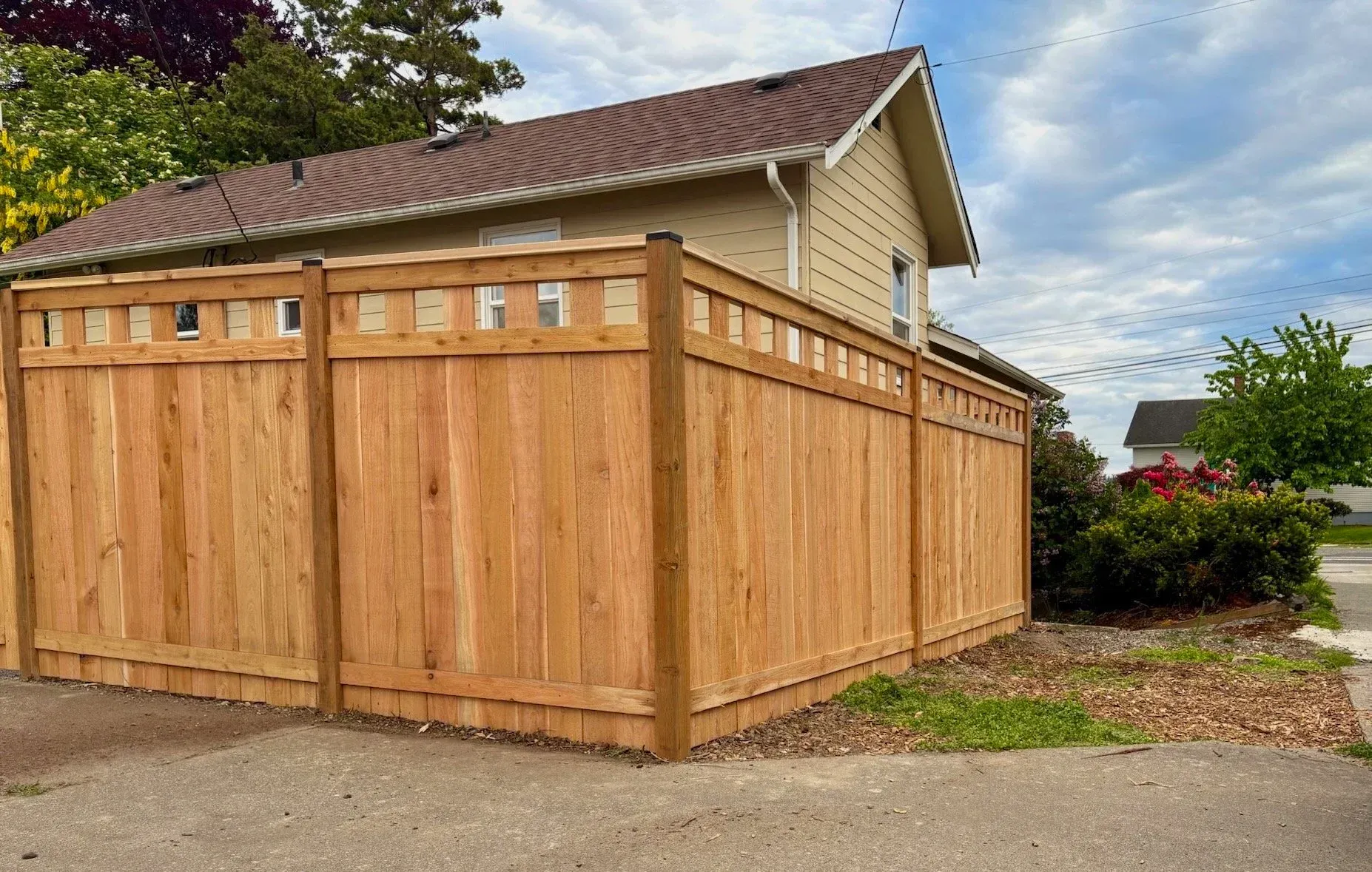 Large wooden privacy fence enclosing a house corner beside a driveway under a cloudy sky