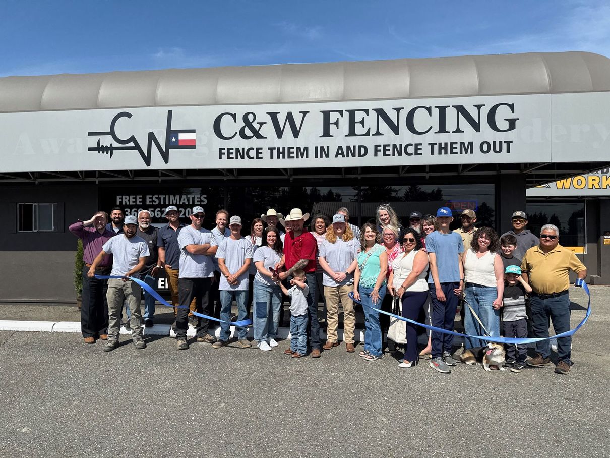 Group posing outside C&W Fencing storefront, holding a blue ribbon during a ribbon-cutting ceremony