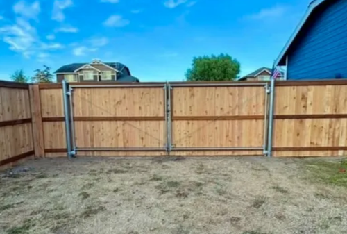 Wooden backyard fence with a double gate and blue house visible behind it.