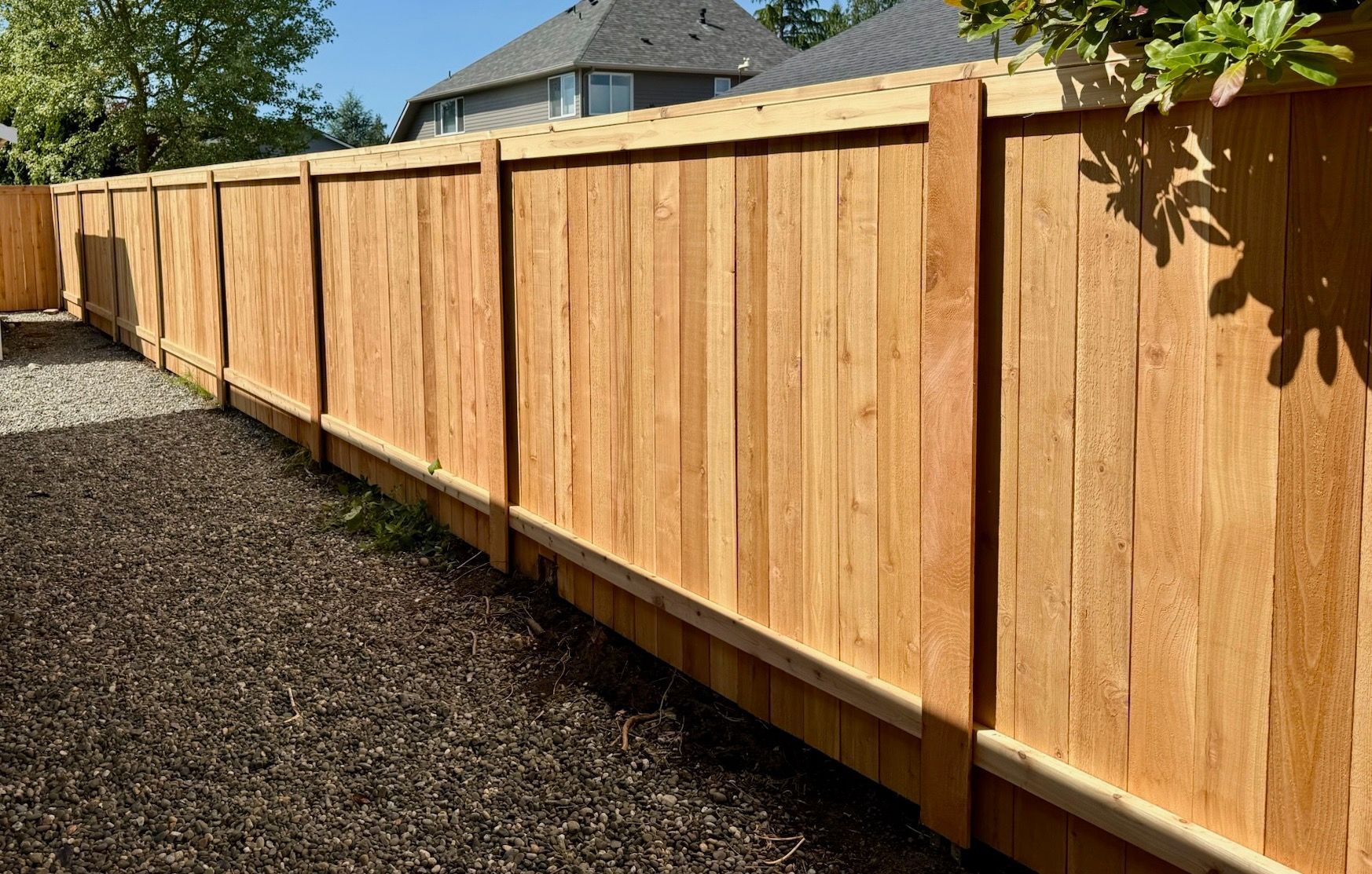 Wooden privacy fence along a gravel yard in bright sunlight