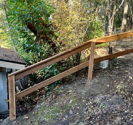Wooden handrail along a sloped outdoor path beside a wooded hillside