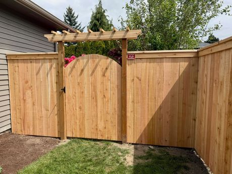 Wooden backyard fence with a central gate and pergola, beside a house and lawn