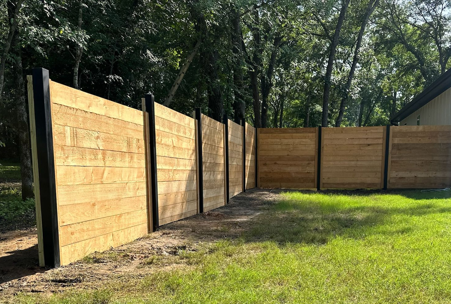 Wooden privacy fence along a grassy yard beside trees in daylight