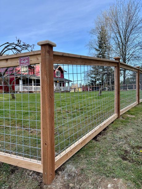 Wooden fenced garden with wire mesh in front of a red building and grassy yard