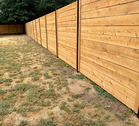 Long wooden fence along a patchy grass yard under trees