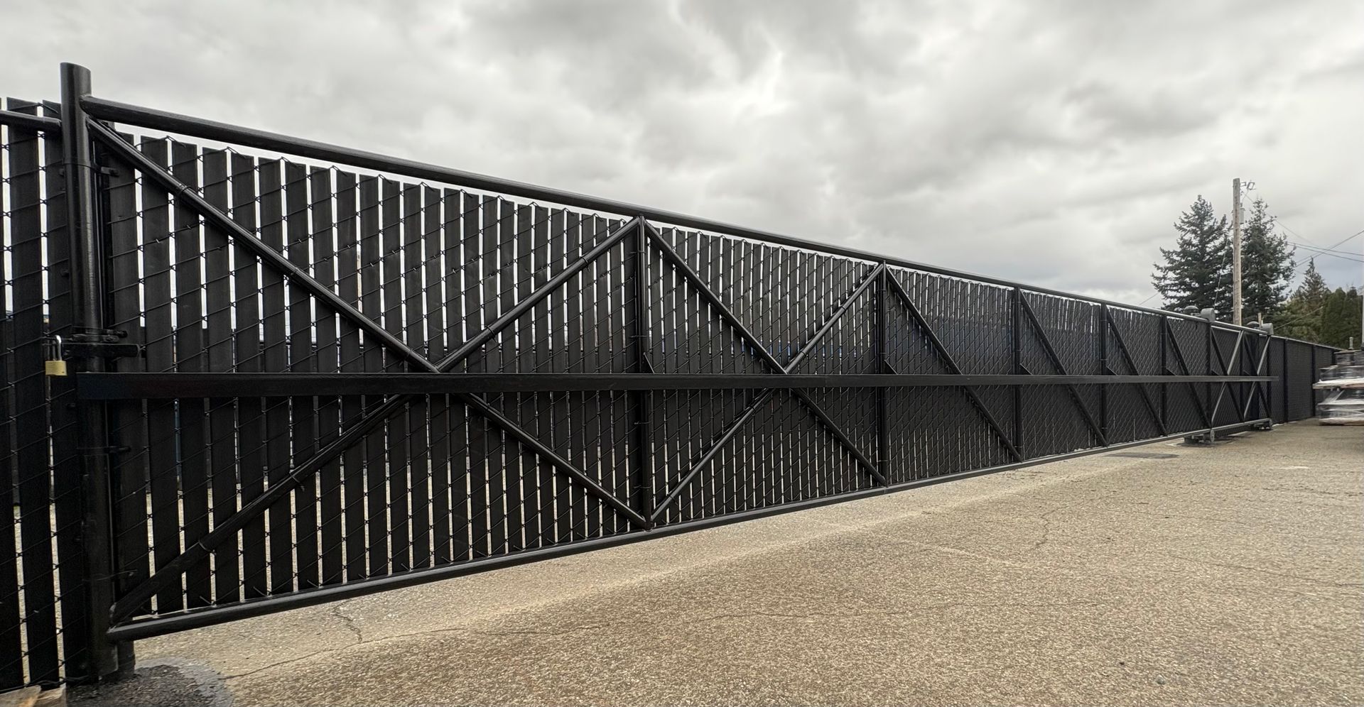 Black metal security gate along a gravel path under a cloudy sky