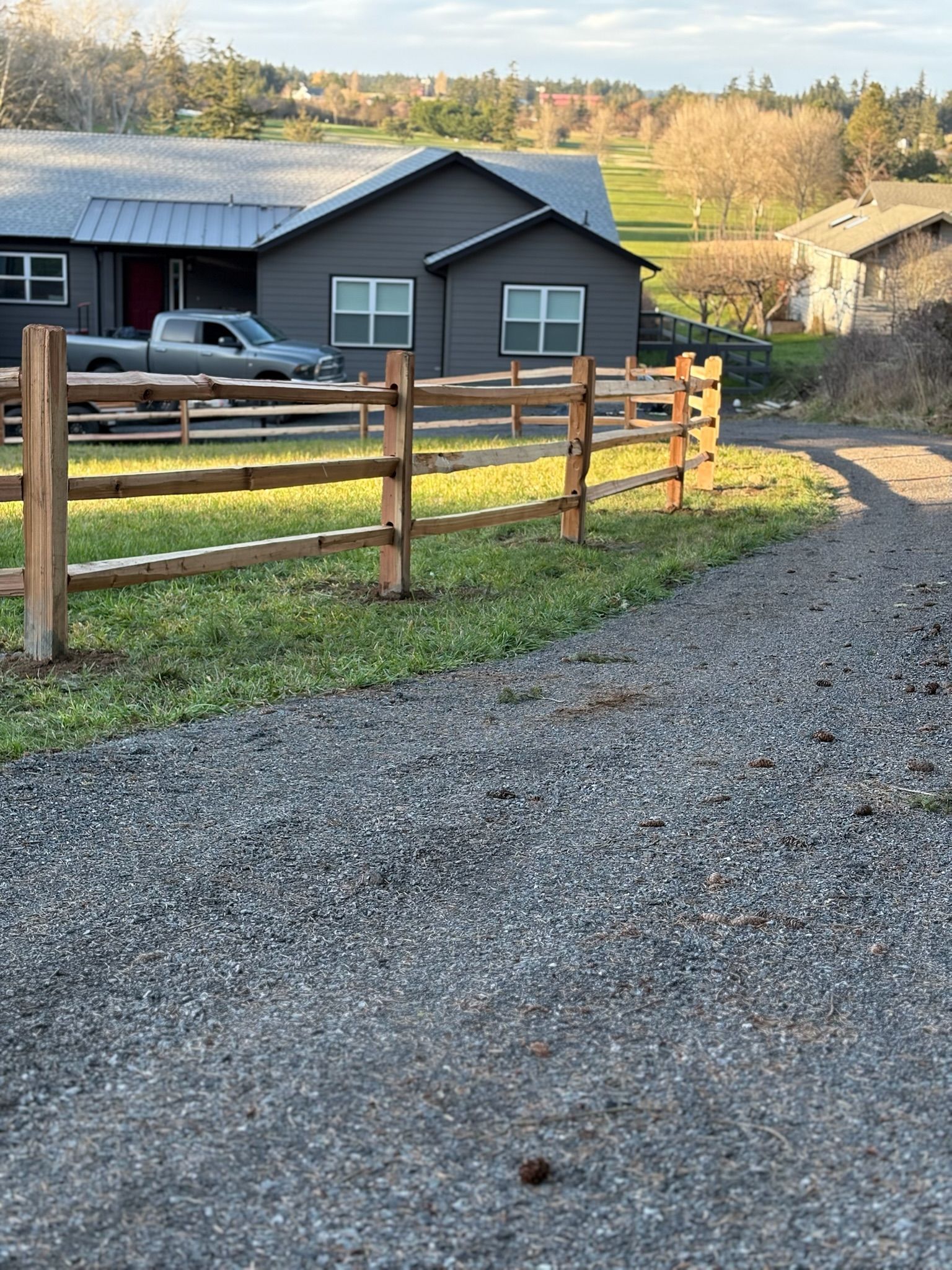 Gravel driveway beside a wooden fence and dark house with a parked truck in a rural yard.