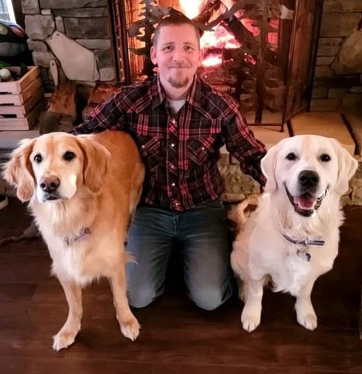 A man kneeling down with two dogs in front of a fireplace