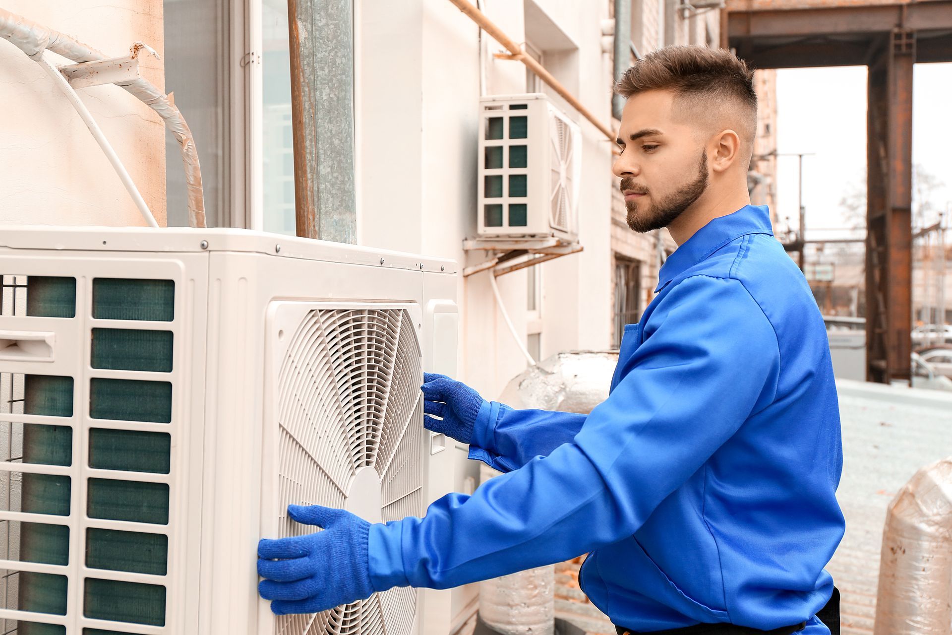 Technician in blue shirt installing or servicing an outdoor air conditioning unit on a building exterior