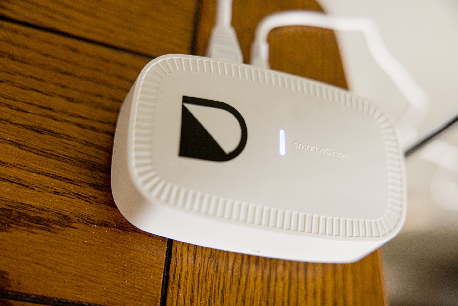 White rectangular device with a black logo and a lit indicator light on a wooden table