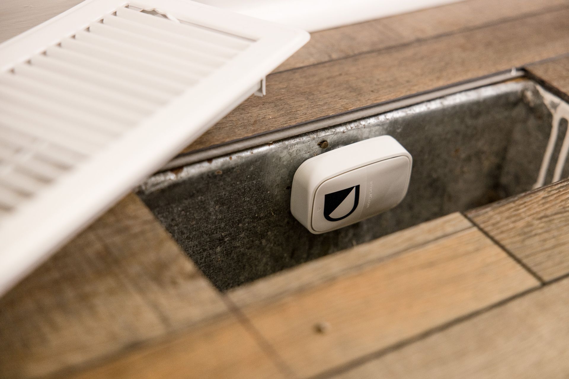 Close-up of a white outlet or cover plate beside a wooden floor and vent grille
