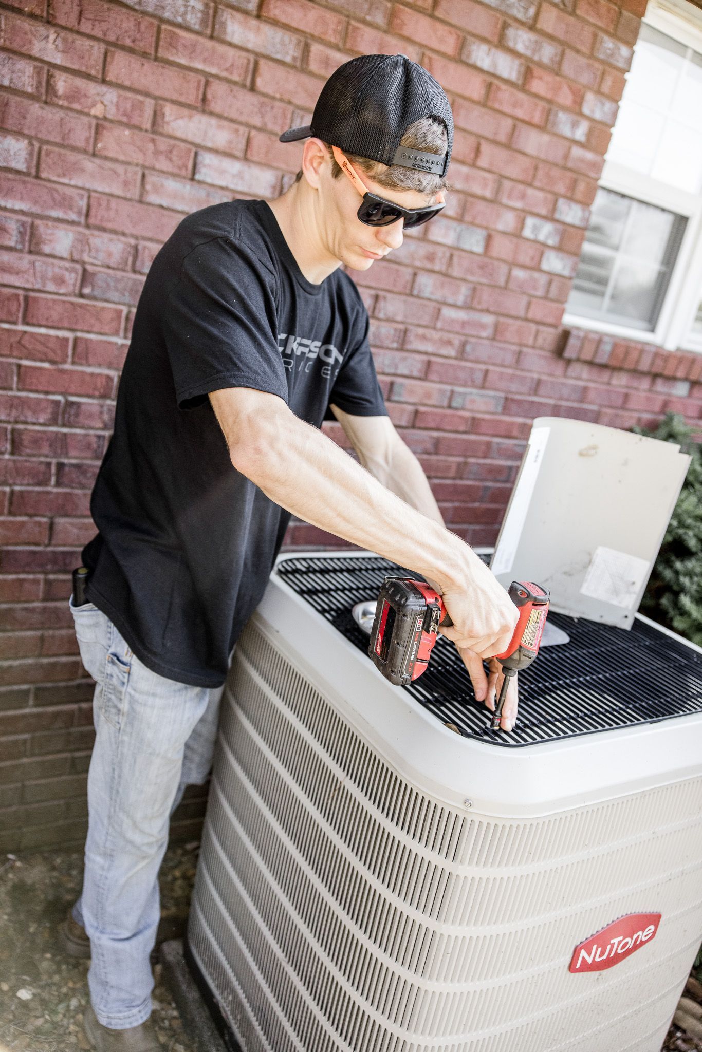 Person working on an outdoor air conditioning unit beside a brick wall