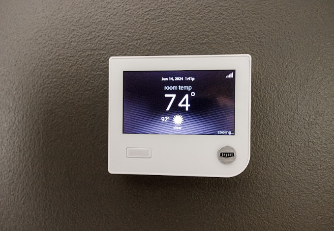 Thermostat on a wall displaying 74° on a dark screen
