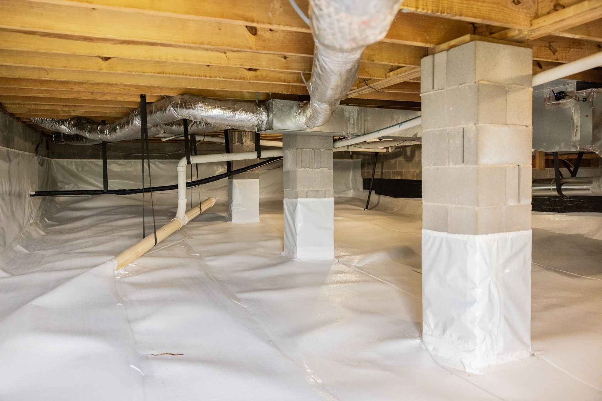 Attic with insulated metal ductwork, wooden framing, and exposed beams over white insulation debris