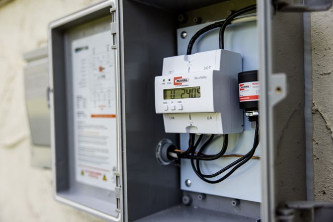 Open electrical meter box with white devices and black cables mounted on a wall
