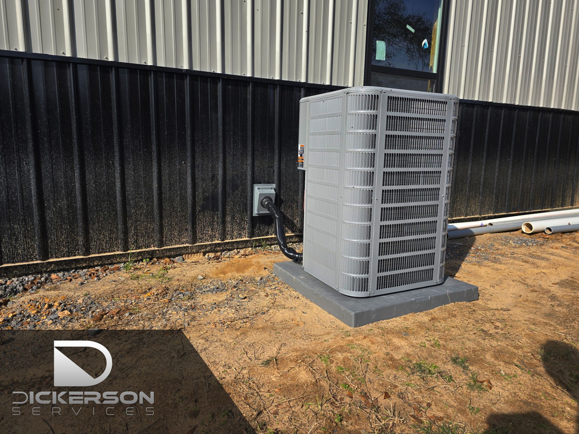Outdoor HVAC unit beside a metal building, enclosed by a gray louvered cage on a concrete pad.