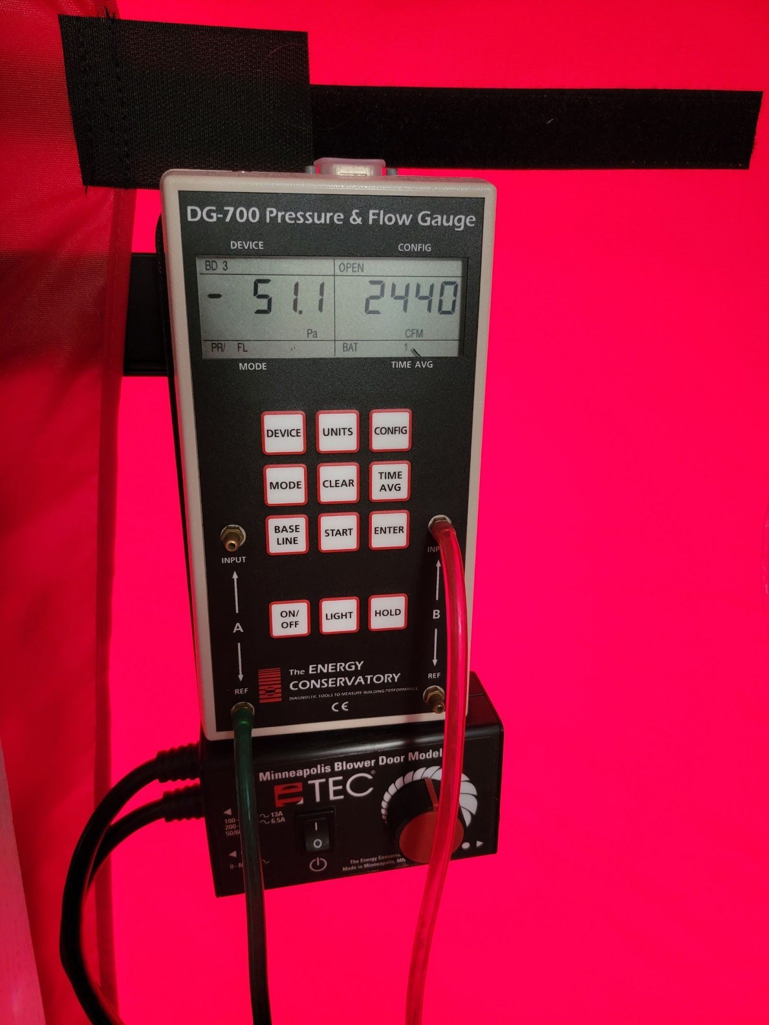 Black digital pressure gauge mounted on red background with cables attached