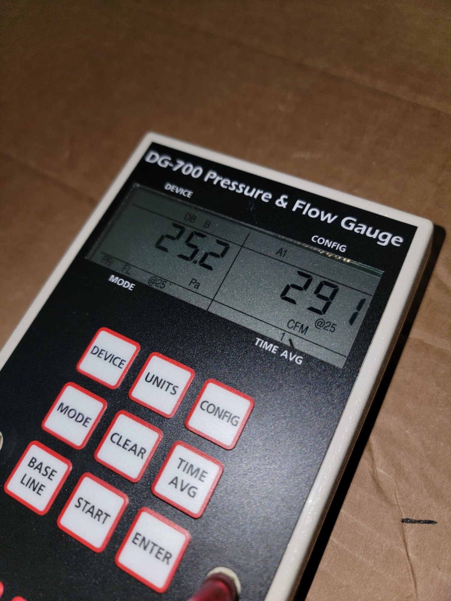 Close-up of a black DG-700 pressure and flow gauge with digital readings on a cardboard surface
