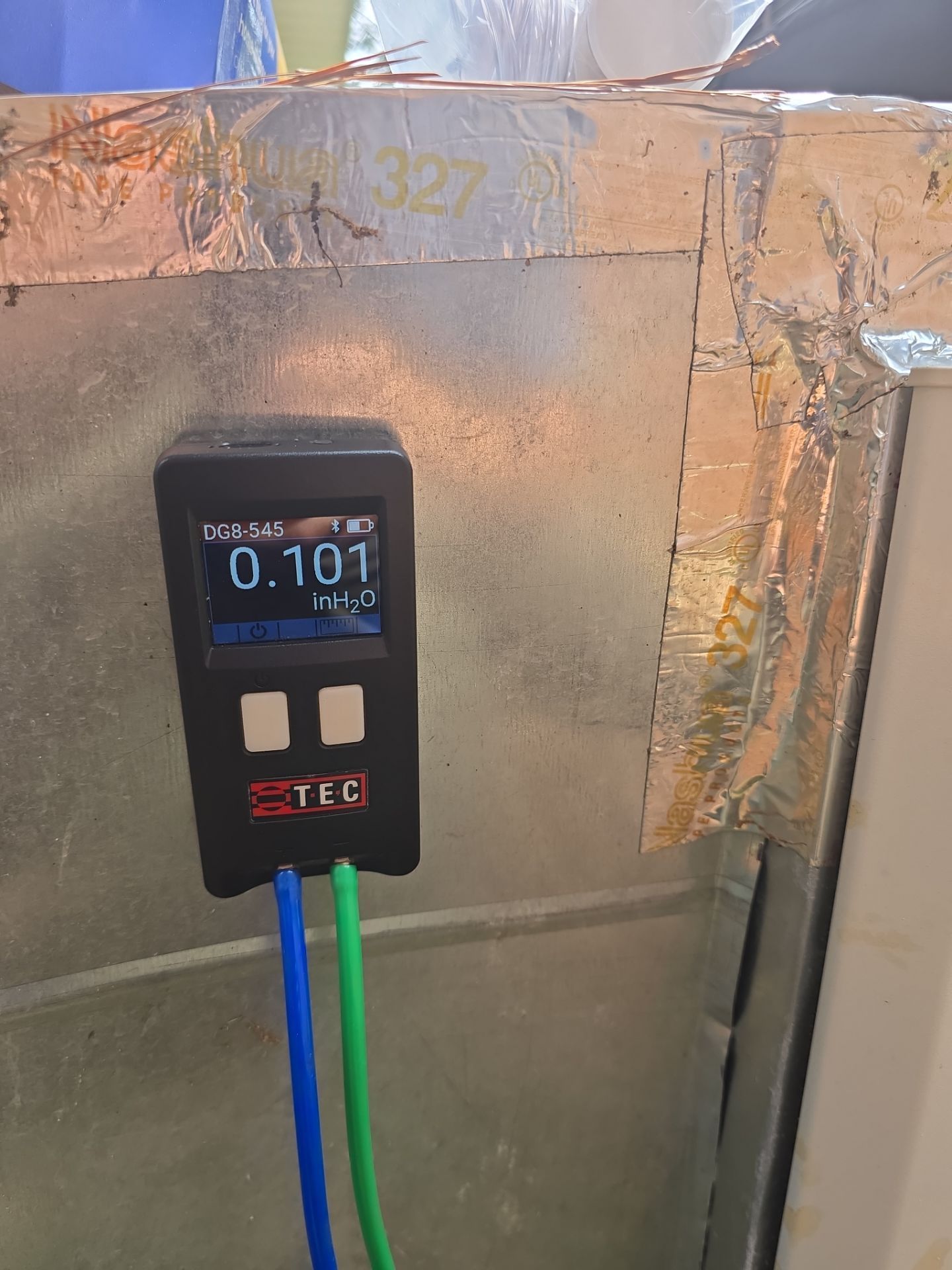 Handheld meter with blue and green cables connected to a foil-covered wall, showing a reading of 0.101.