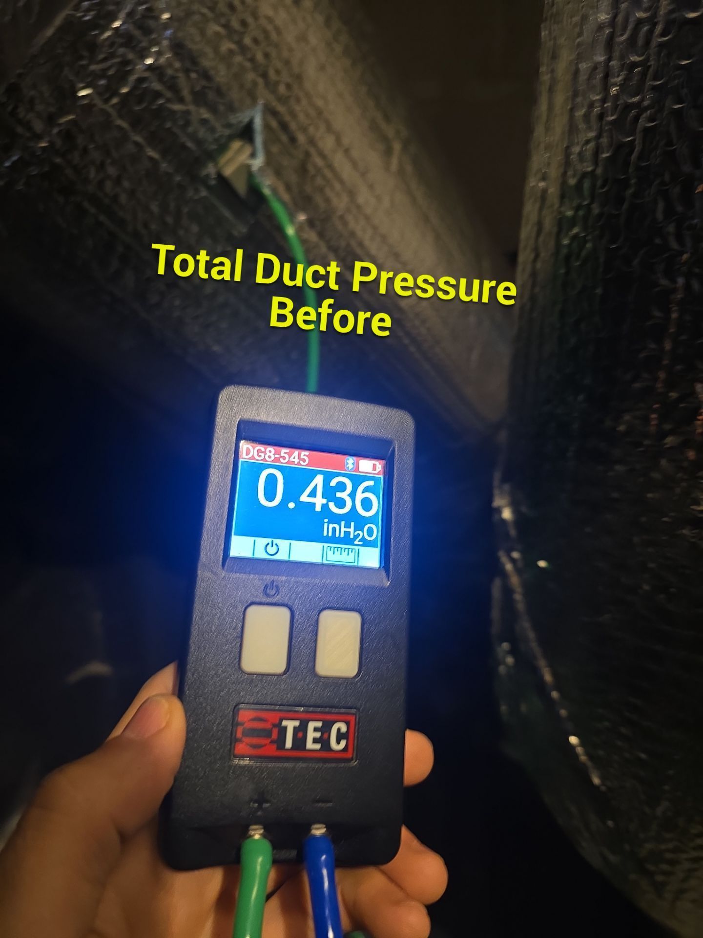 Technician measuring total duct pressure with a digital meter in an HVAC duct, reading 0.436.