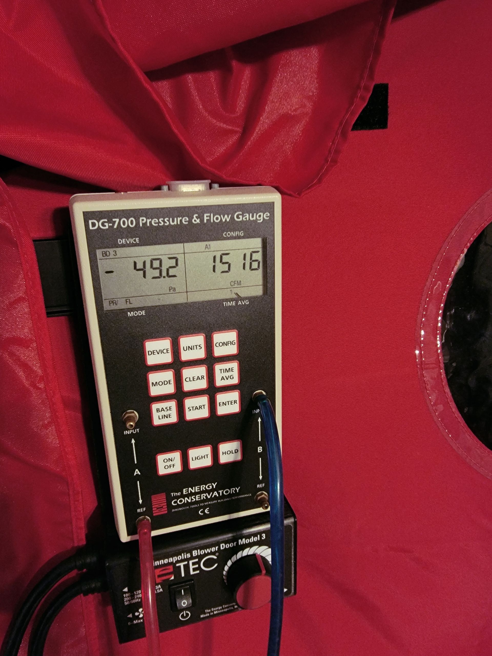Digital handheld meter in a red carrying case displaying readings on its screen.