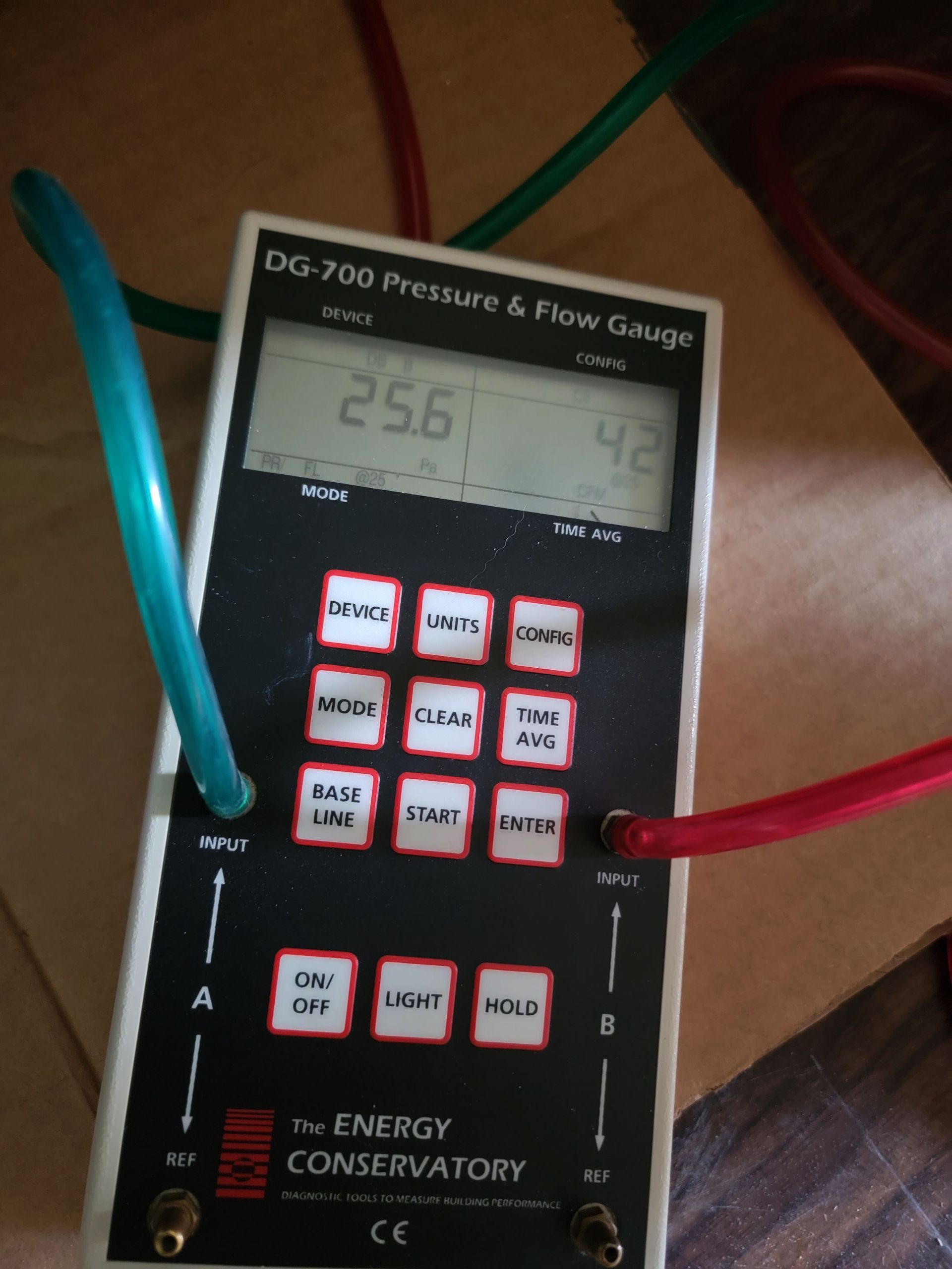 Portable pressure and flow gauge with blue and red hoses attached, showing a digital reading.