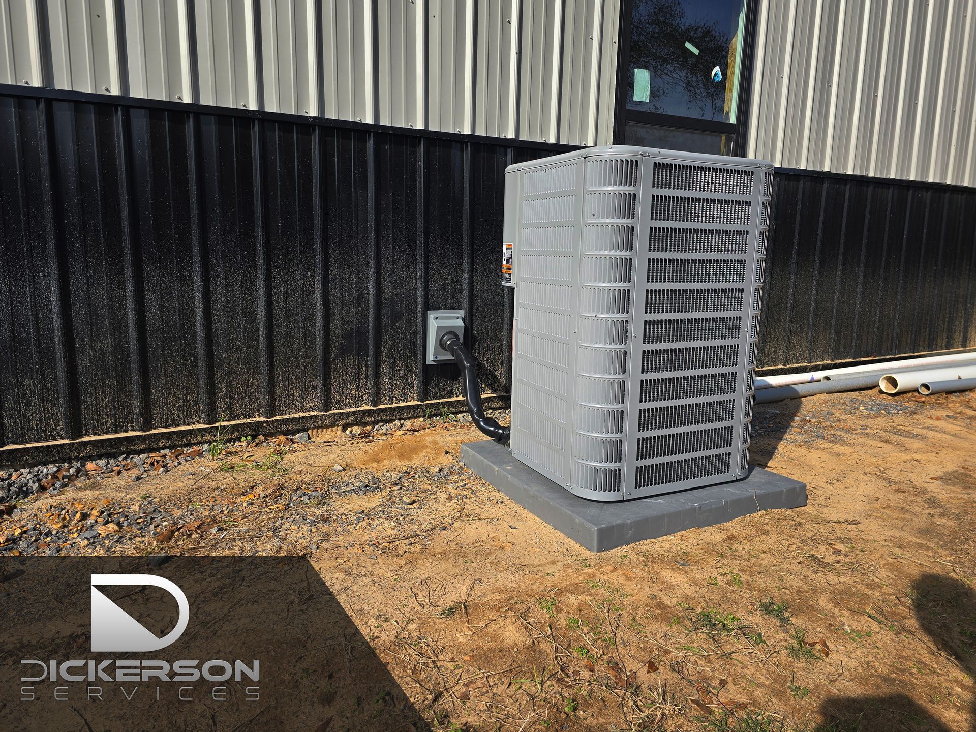 Gray outdoor HVAC unit beside a metal-sided building on a concrete pad in a dirt lot