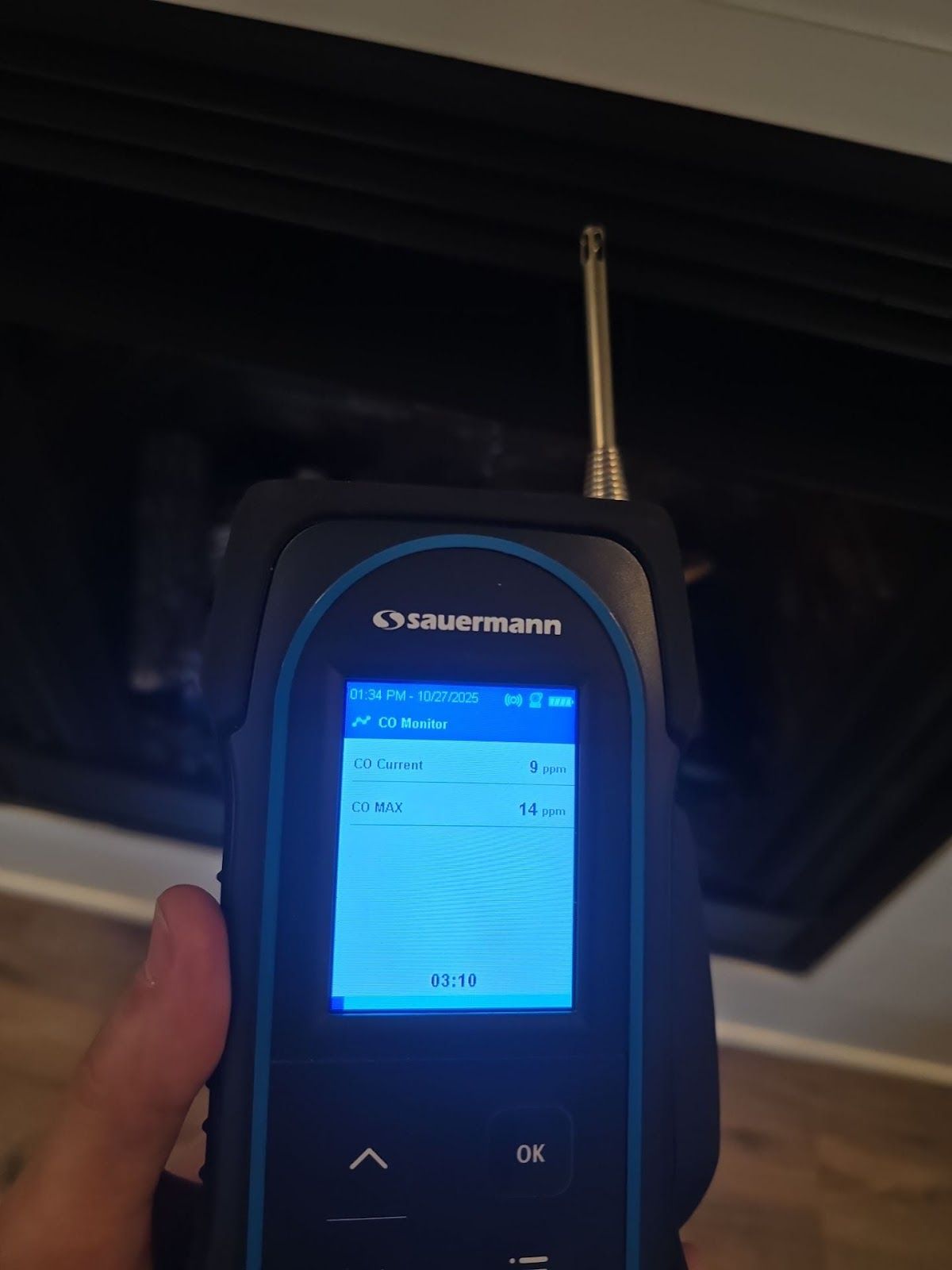 Handheld Garmin device displaying a blue-lit menu screen, held up indoors under a dark ceiling