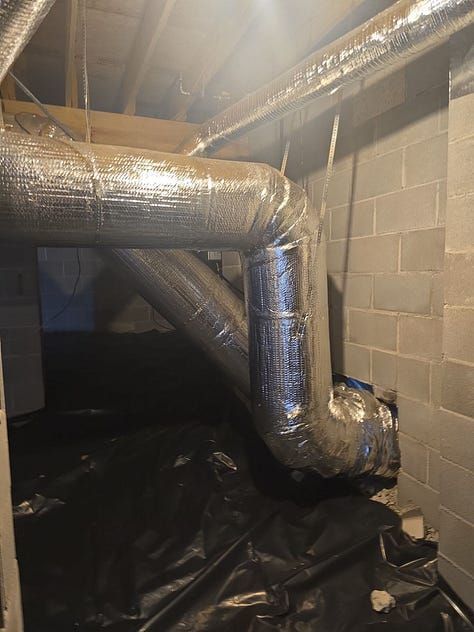 Insulated ductwork and pipes in a dim basement utility space with cinder block walls.