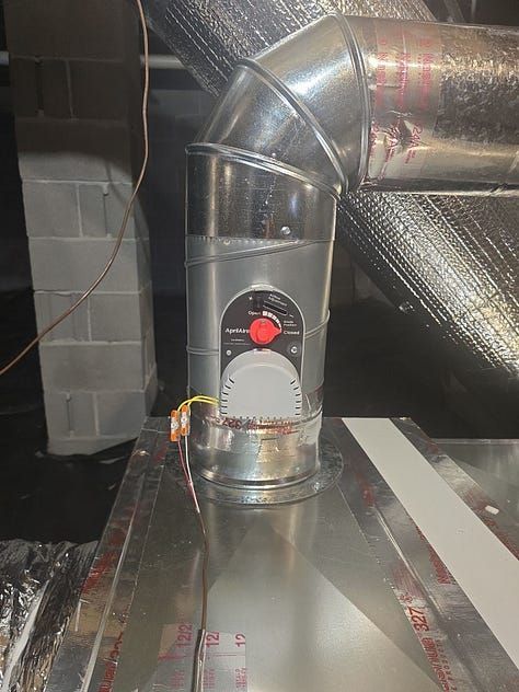 Metal HVAC duct with a round red control unit attached in an attic-like space.