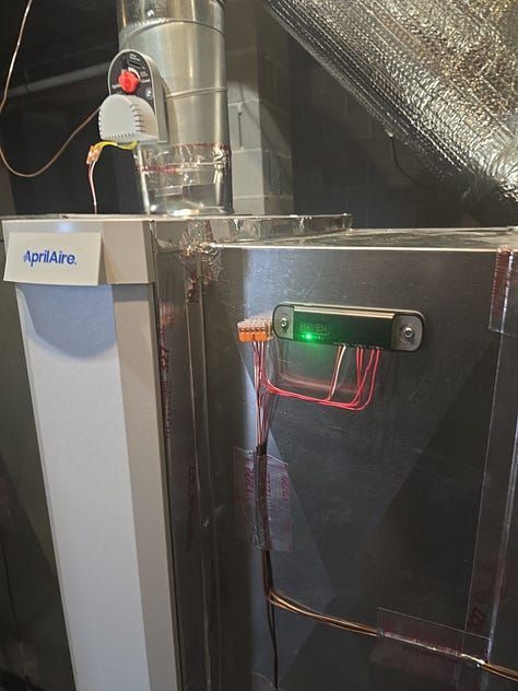 Metal ductwork with a green-lit sensor device mounted on a reflective wall in an attic or utility space