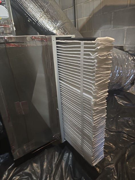 White HVAC filter leaning in an industrial room with ductwork and black plastic sheeting.