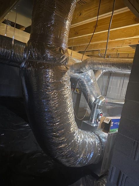 Black insulated HVAC ducts and exposed wooden ceiling in an attic or crawl space.