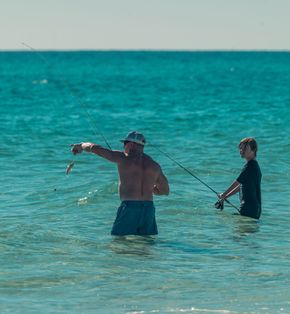 Two people fishing in turquoise ocean water, one holding up a caught fish.