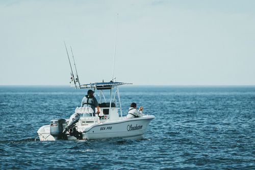 White fishing boat with anglers on calm blue ocean under a pale sky