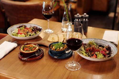 Restaurant table with red wine, bread, and several plated salads and appetizers