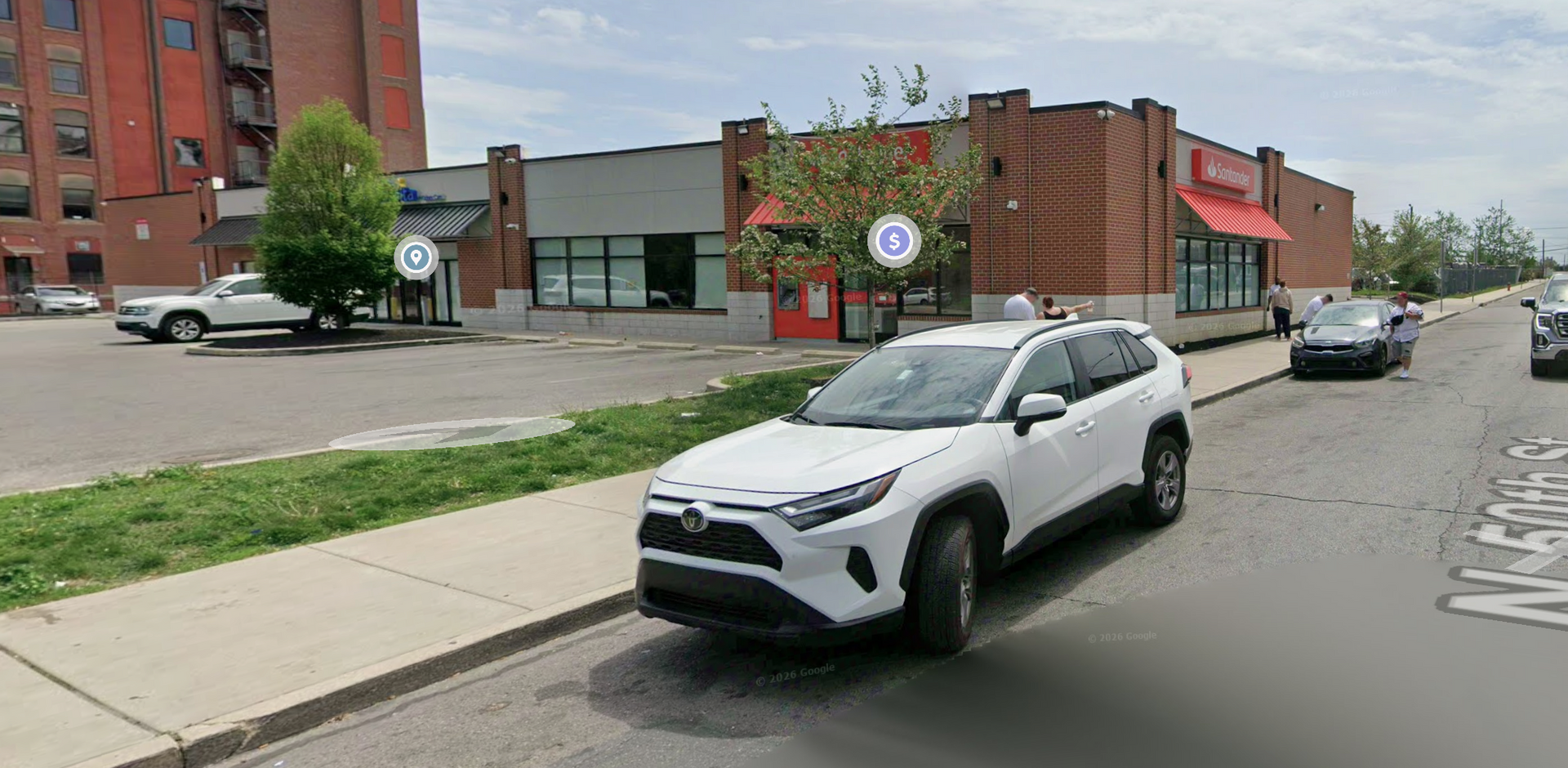 A white SUV parked on a city street in front of a brick commercial building with red awnings and blue circular signs.