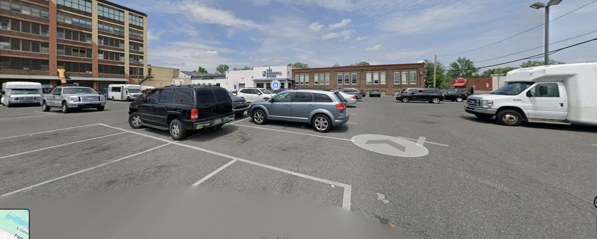 A wide-angle view of a parking lot featuring various cars parked near brick buildings on a sunny day.