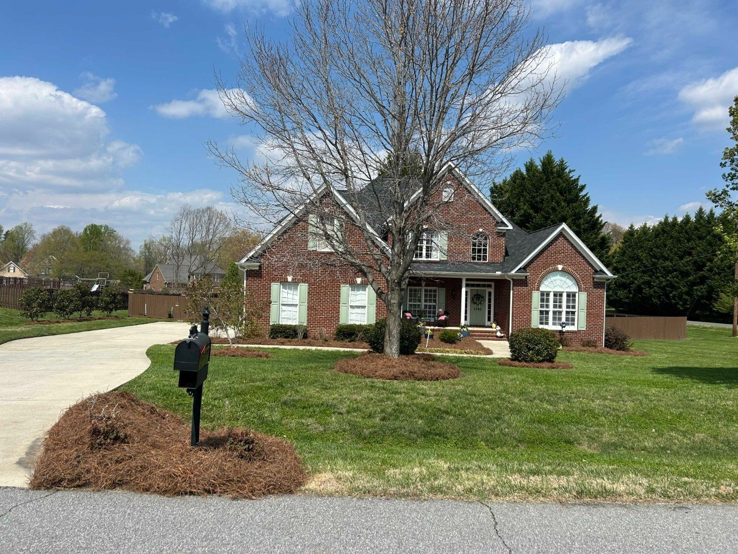 Brick house with white trim and a front yard, driveway, and mailbox under a partly cloudy sky