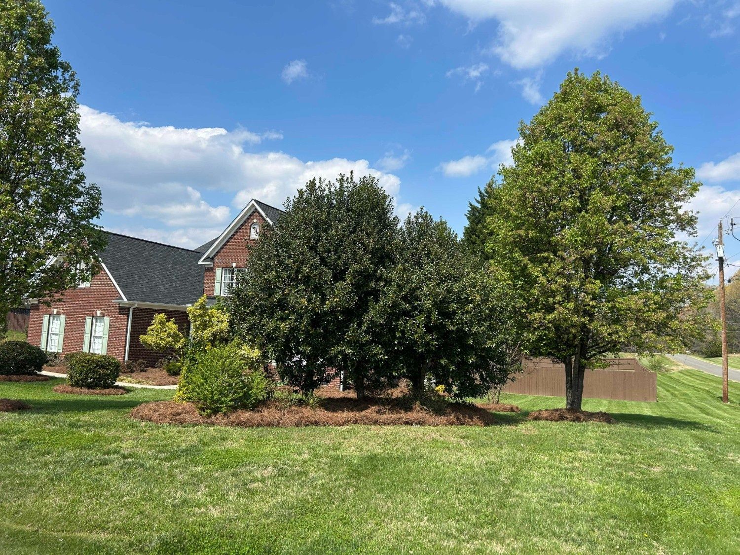 Brick house with trees and a green lawn under a blue sky