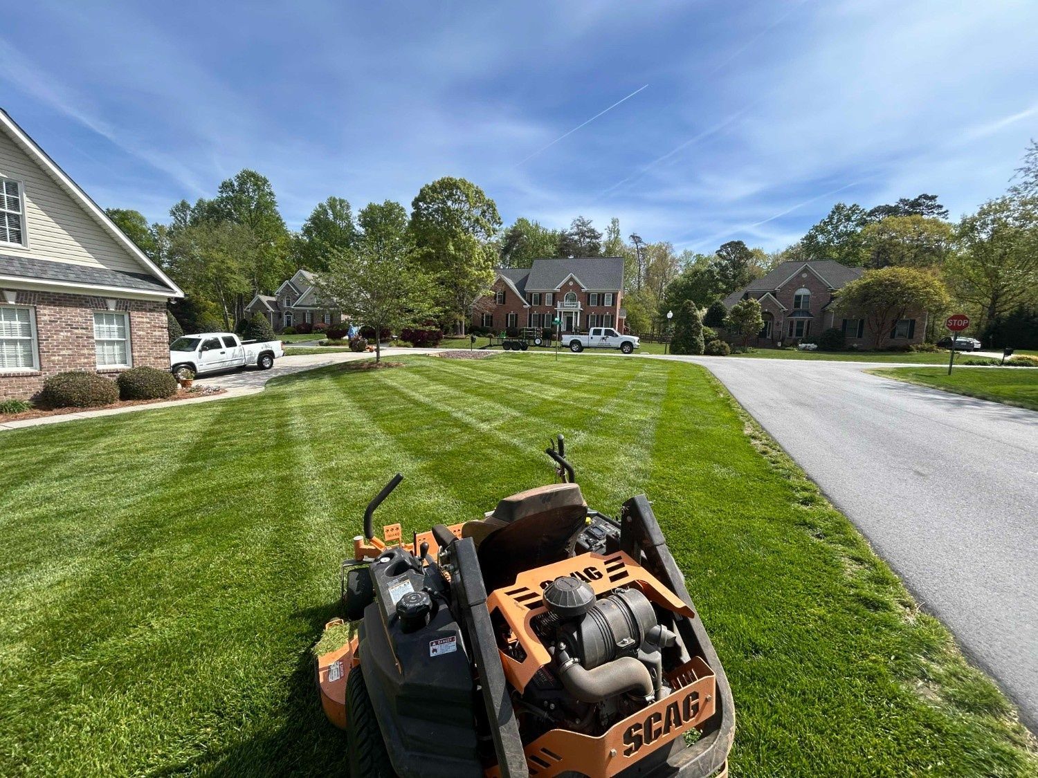 Orange lawn mower on a suburban street with a striped green lawn and houses in the background