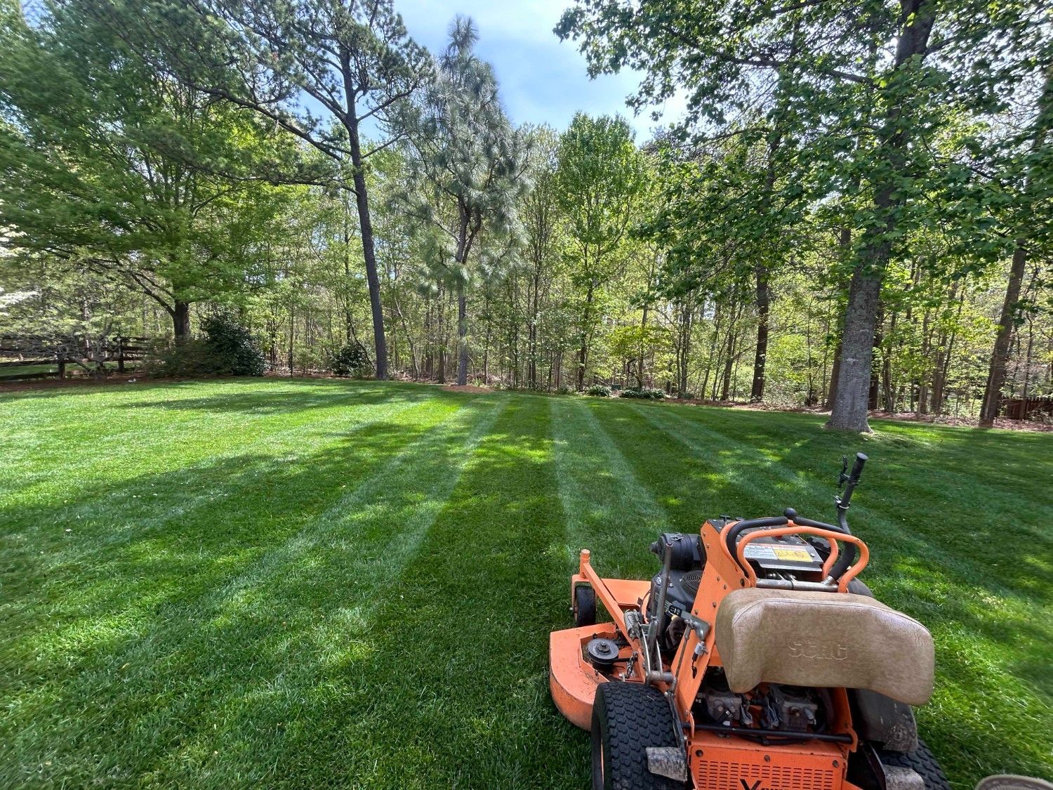 Lawn mower cutting a sunlit green lawn with trees in the background