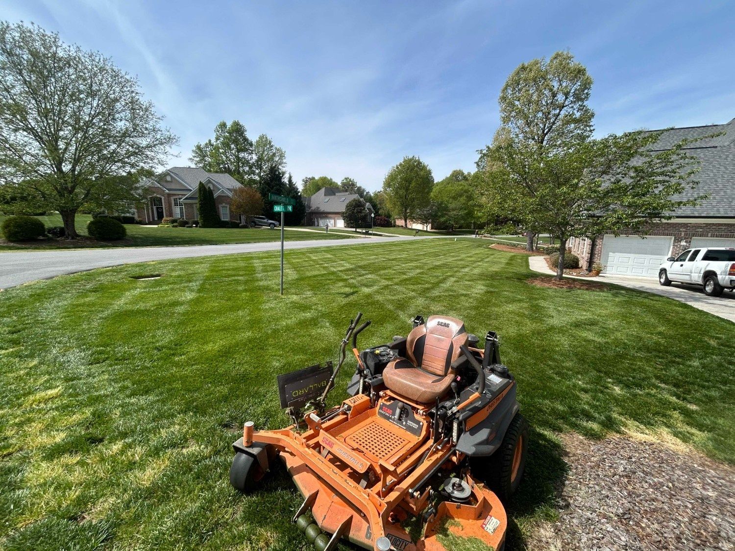 Orange lawn mower in a green suburban yard with houses and trees in the background