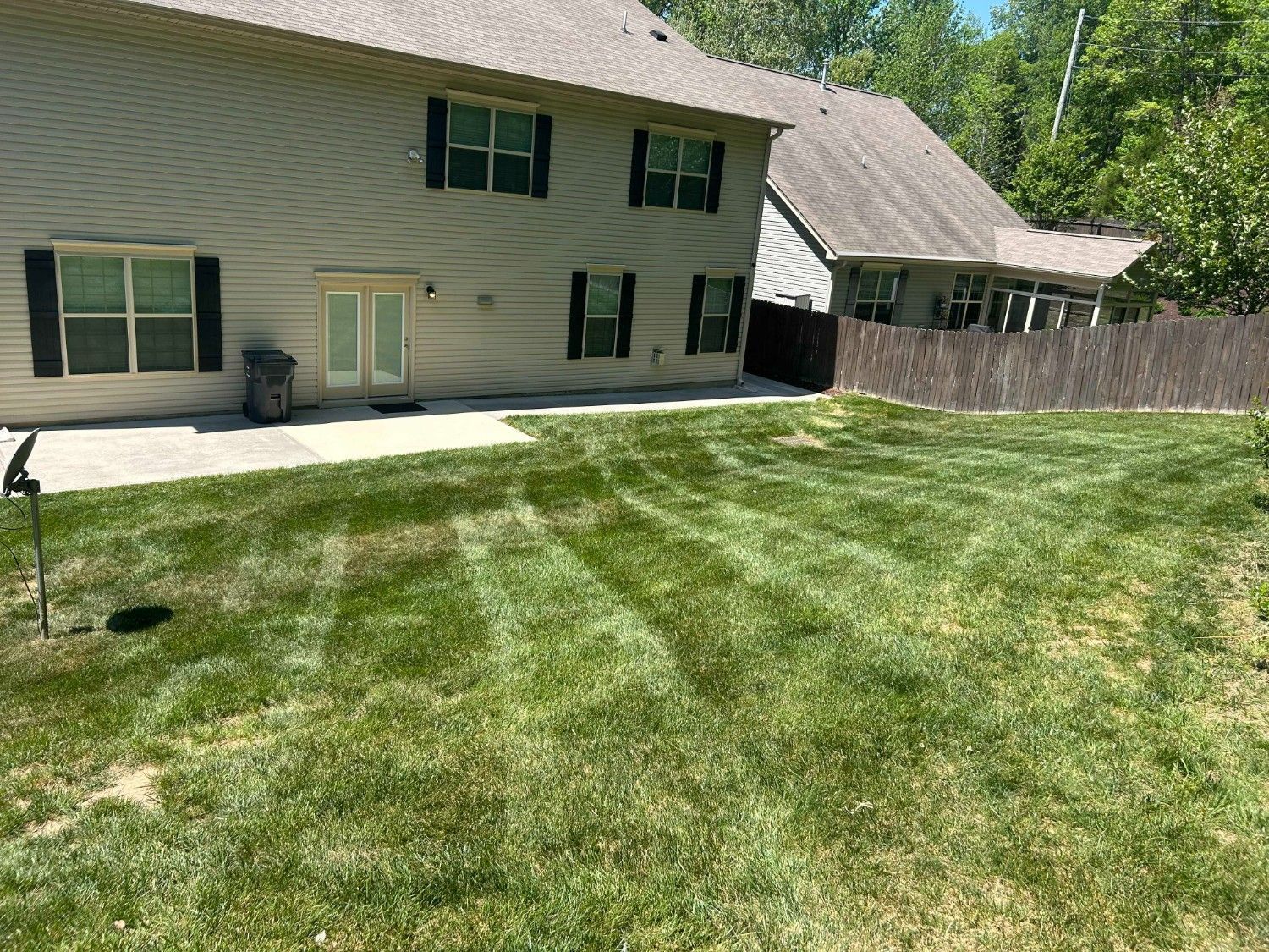 Backyard with green lawn beside a beige house and wooden fence in bright sunlight