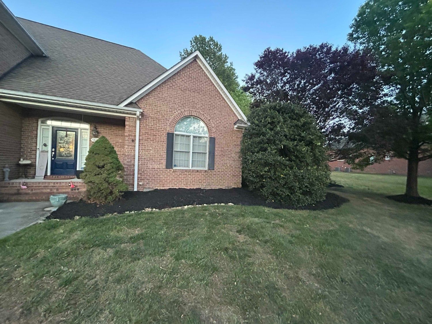 Brick suburban house with arched window, lawn, shrubs, and trees in front yard