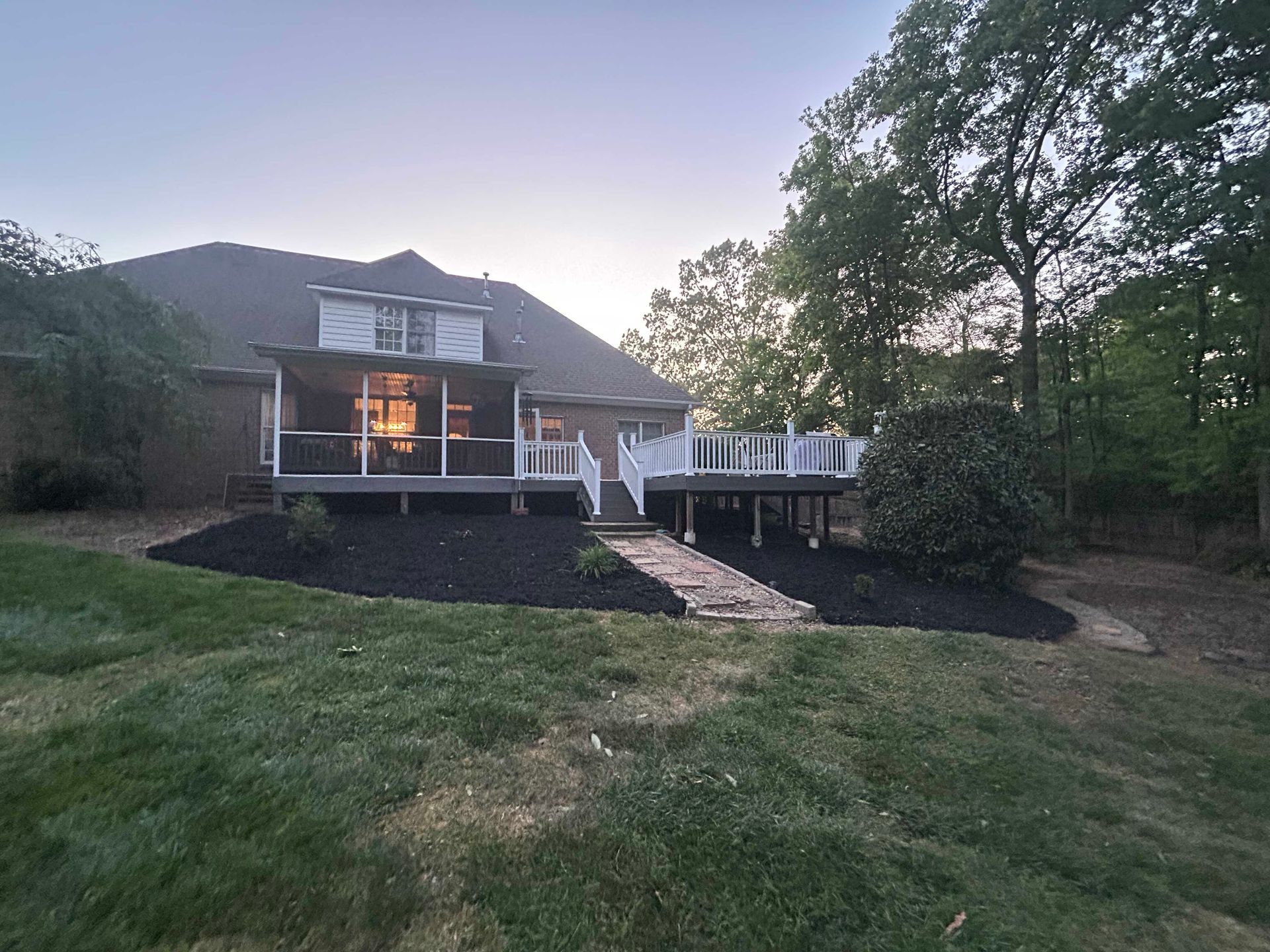 Suburban house with deck and stairs, seen across a grassy yard at dusk