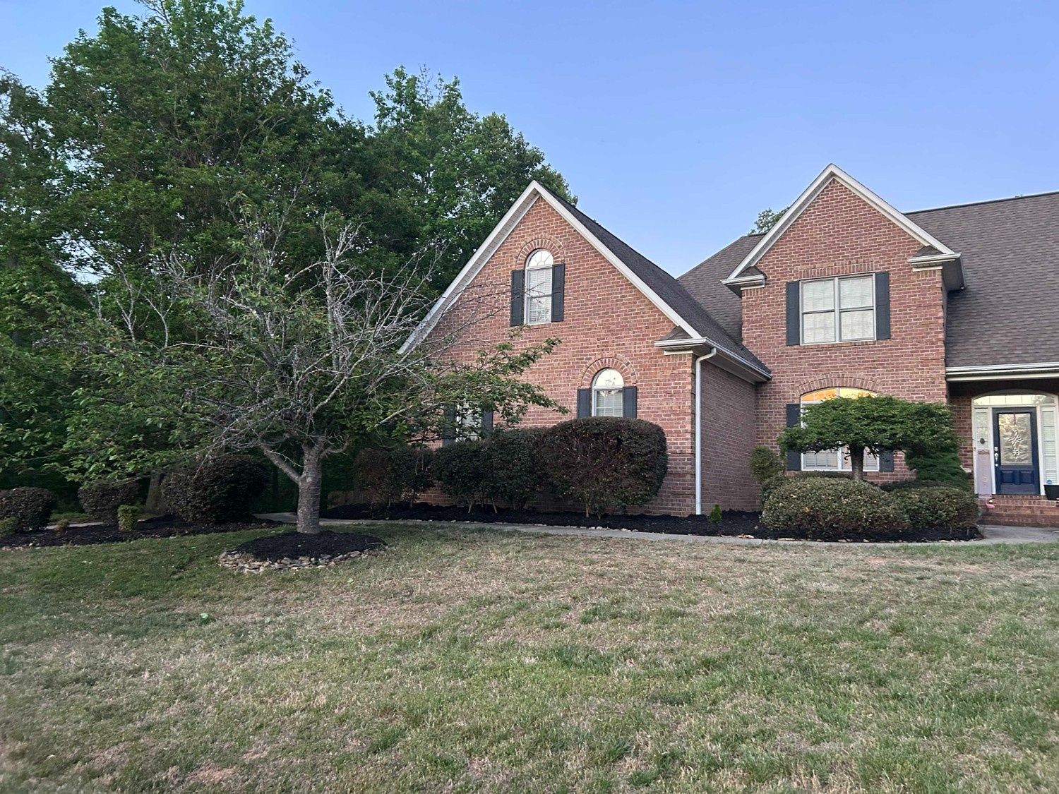 Brick suburban house with steep gables, front lawn, and large tree beside the driveway